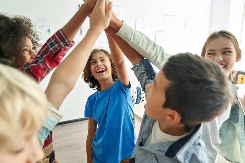 A circle of multi-ethnic children holding handing up high together 